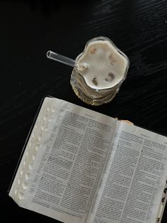 an open book sitting on top of a table next to a glass filled with liquid