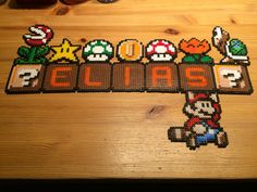 a wooden table topped with an image of mario and other characters on the word spelled out in perler beads