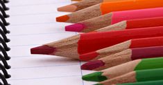 several colored pencils lined up in a row on top of a notepad with writing paper next to them