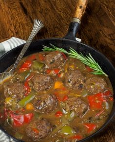 a skillet filled with meatballs, peppers and carrots next to a fork