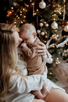 a woman holding a baby in front of a christmas tree