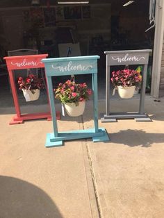 two small mirrors with flowers in them on the sidewalk next to a street sign that says welcome