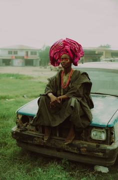 a woman sitting on the hood of a car with a pink turban over her head