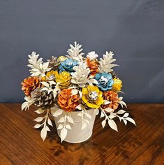 a white vase filled with colorful flowers on top of a wooden table