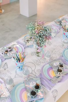 a table set up with plates, cups and vases on it for an unicorn themed party