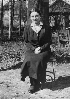 an old black and white photo of a woman sitting on a chair next to a tree