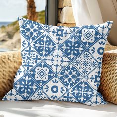 a blue and white pillow sitting on top of a couch next to a wicker chair