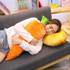 a woman is laying on a couch with a large carrot pillow