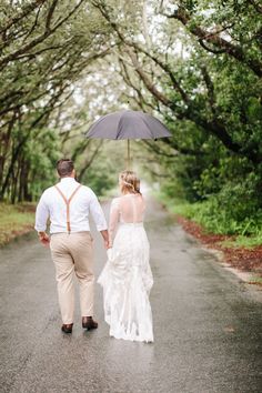 a bride and groom walking down the road under an umbrella