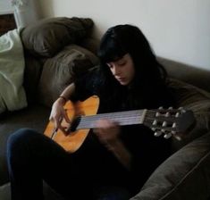 a woman sitting on a couch playing an acoustic guitar