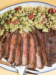 a plate with steak, avocado and tomato salad on it next to two forks