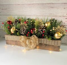 a wooden box filled with pine cones and greenery on top of a white table