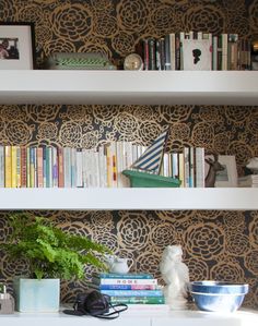 the bookshelves are full of books and vases with plants on them in front of decorative wallpaper