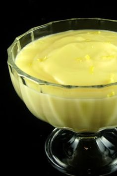 a glass bowl filled with yellow liquid on top of a black table next to a spoon