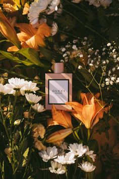 an arrangement of flowers with a perfume bottle in the middle surrounded by white and orange flowers