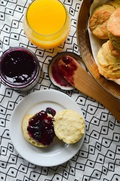 some biscuits and jam are on a plate next to a glass of orange juice in a bowl