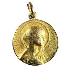 A French 18 karat (18K) yellow gold charm pendant designed as a round medal with a relief of the Virgin Mary in profile with a halo, with the Latin motto 'VIRGO VIRGINUM' (Virgin of Virgins) surrounding. The reverse depicts the letter M on a cloud with a sheaf of roses in front of a sunburst and the engraved monogram EJ and the date 23 Mai 1930. Stamped with the eagle's head for 18 karat gold and French manufacture, along with an incomplete maker's mark.  Dimensions: 2.1 x 1.8 x 0.175 cm (not including jump ring) Weight: 4.84 grams (Chain not included) Latin Mottos, The Virgin Mary, Eagle Head, Maker's Mark, Pendant Design, Gold Charm, Virgin Mary, Makers Mark, Charm Pendant