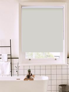 a white bath tub sitting next to a window in a bathroom with tiled floors and walls