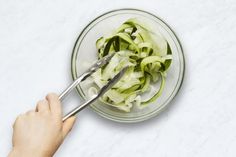 a person cutting up some food in a glass bowl with a knife and tongs