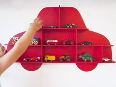 a child's hand reaching up to a red shelf with toy cars on it