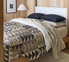 a bed with two pillows on top of it next to a night stand and lamp