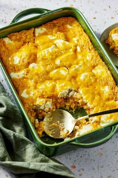 a green casserole dish filled with food next to two spoons on a table