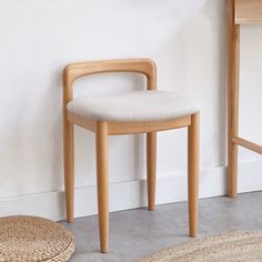 a wooden chair next to a white wall with a round rug on the floor in front of it