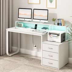 a white desk with two computer monitors and a phone on it next to a plant