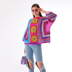 a woman is wearing a colorful crochet sweater and ripped jeans, holding a handbag