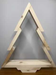 a wooden triangle shaped shelf on top of a hard wood floor next to a gray wall