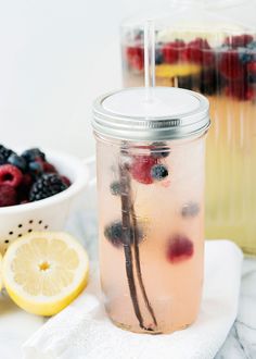 a mason jar filled with lemonade and berries next to a bowl of raspberries