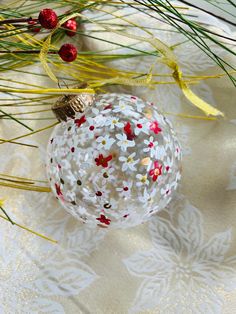 a glass ornament sitting on top of a table next to pine needles and red berries