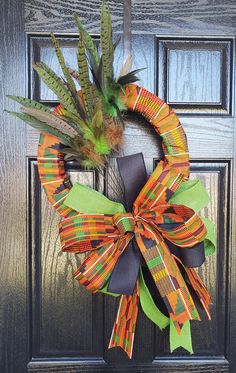 an orange and green wreath is hanging on the front door, with feathers attached to it