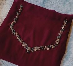 a necklace is laying on top of a red cloth with gold flowers and leaves attached to it