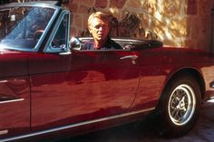 a man sitting in the driver's seat of a red sports car