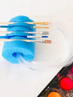 the paint brushes are next to some watercolors in a plastic container with a blue towel