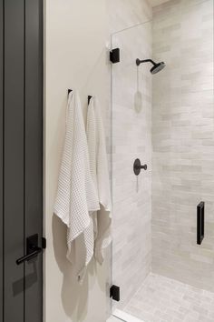 two towels hanging on the side of a glass shower door next to a white tiled wall