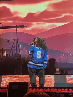 a woman standing on top of a stage in front of a large screen with a sky background