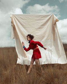 a woman in a red dress is walking through tall grass with a white sheet over her head