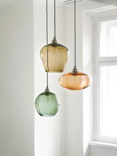 three different colored glass pendant lights hanging from a ceiling fixture in a room with white walls