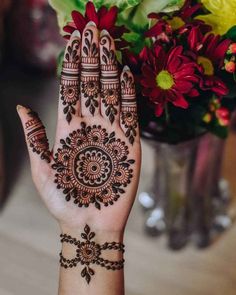 a woman's hand with henna tattoos on it and flowers in the background