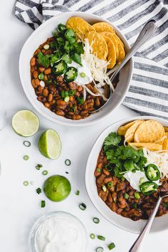 two white bowls filled with beans and tortillas topped with sour cream, cilantro, jalapenos