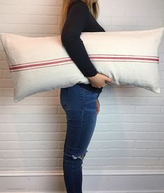 a woman holding a large pillow in front of a white brick wall with red stripes