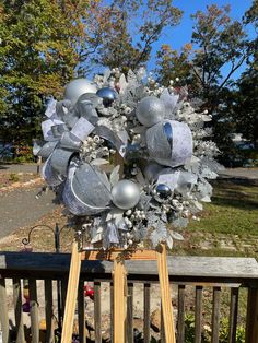 a wreath with silver and white decorations on top of a wooden stand in front of some trees