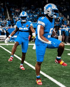 two football players in blue uniforms are running on the field with their feet spread out