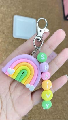 a hand holding a keychain that has a rainbow on it and letters in different colors