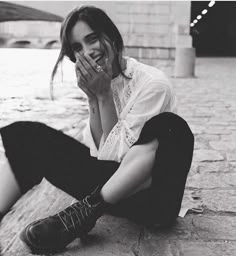 a woman sitting on the ground with her hand over her mouth and looking at the camera