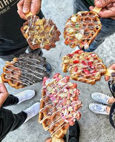 four people holding waffles with toppings on them in front of each other