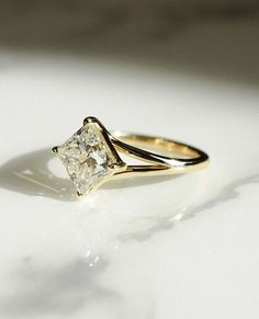 a yellow gold engagement ring with a princess cut diamond in the center on a white surface