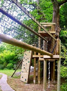 a wooden play set in the middle of a wooded area with climbing bars and ladders